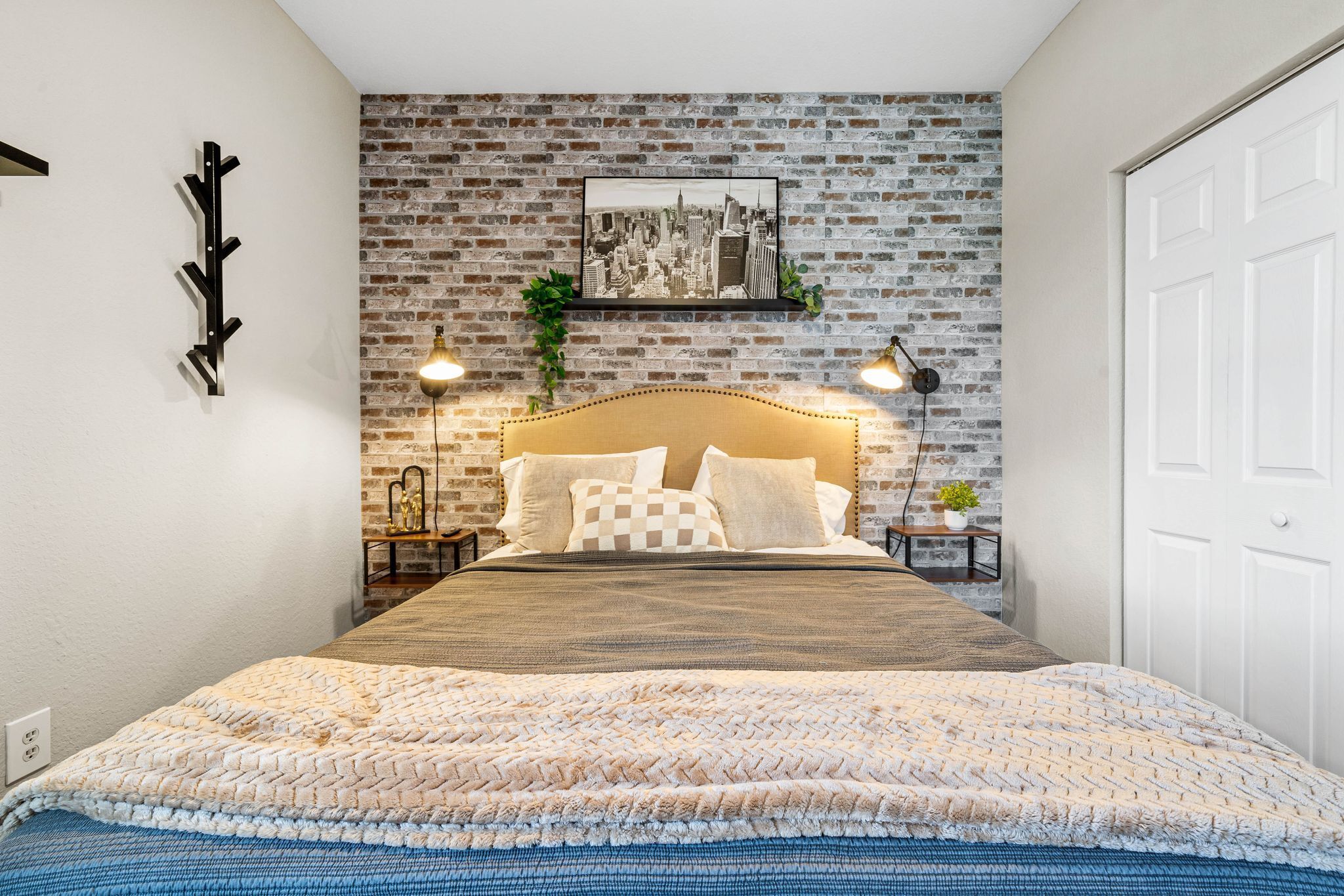 Un dormitorio con pared de ladrillos, una cama con cabecera de madera, dos lámparas de noche y una fotografía enmarcada de un paisaje urbano sobre la cama.