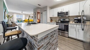 Una cucina moderna con mobili bianchi, una grande isola centrale, elettrodomestici in acciaio inossidabile e una parete decorata con mattoni.