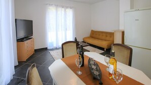 Ein modernes Wohnzimmer mit Flachbildfernseher, Sofa, Esstisch mit Weingläsern und einem Kühlschrank.