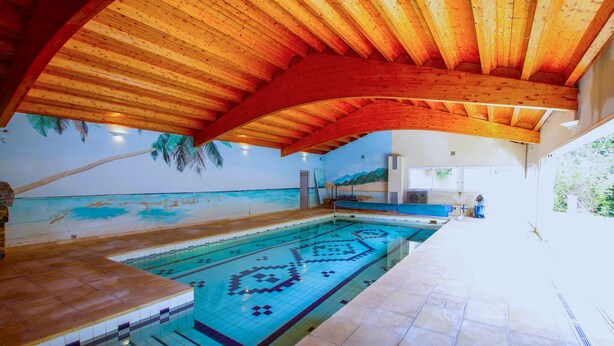 Ein Hallenbad mit Holzbalkendecke und Wandgemälde mit Strandmotiv.