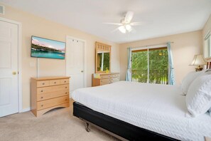 A bedroom with a bed, dresser, TV, ceiling fan, and a window with a view.