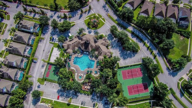 An aerial view of a residential area with a central swimming pool, tennis courts, and a landscaped park.