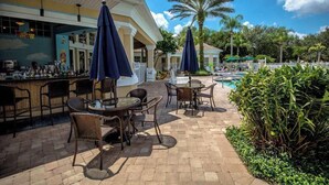 An outdoor bar area with wicker furniture and umbrellas, a pool, and palm trees.