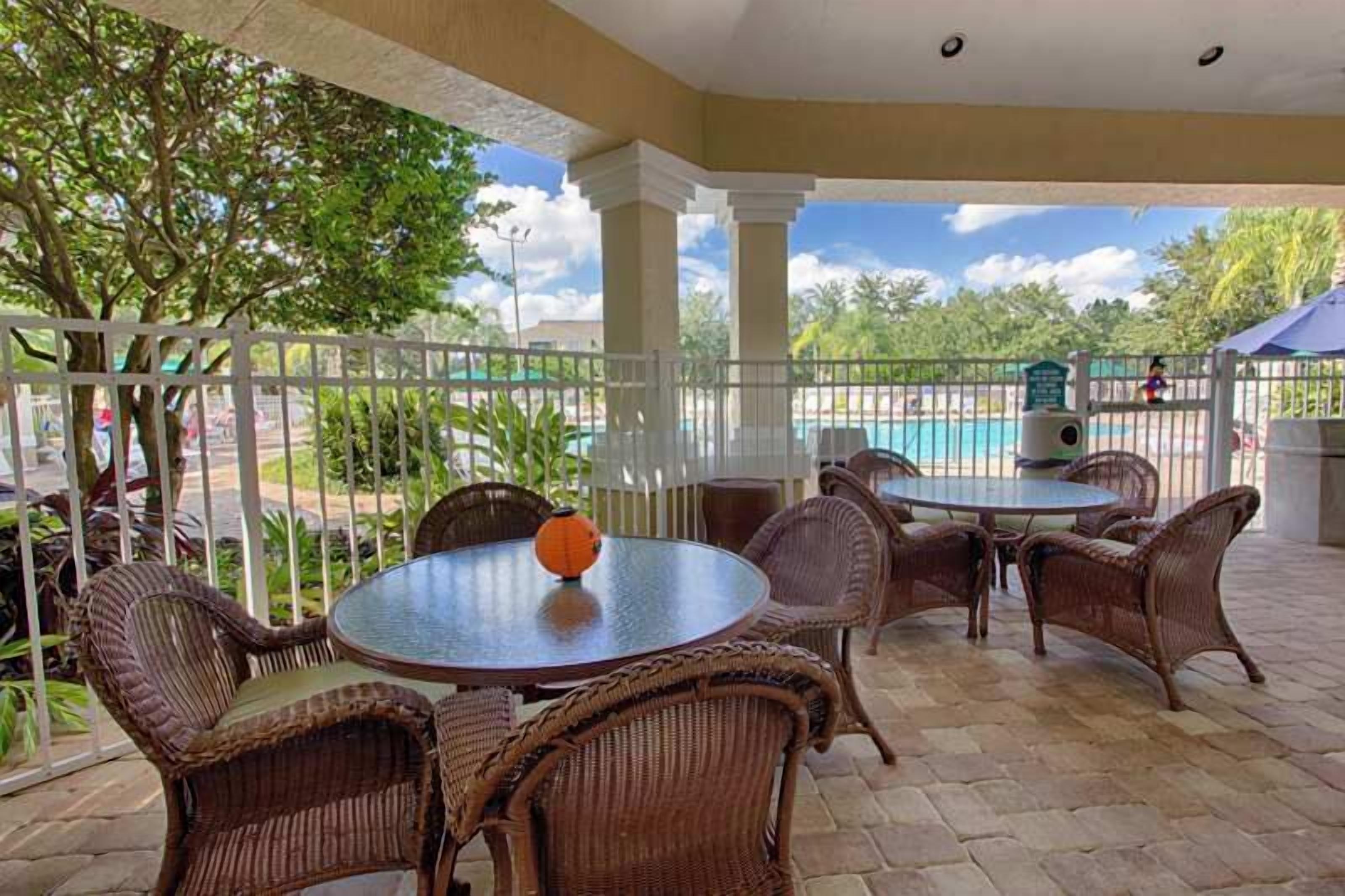 Un patio cubierto con mobiliario de mimbre, una mesa redonda y vistas a una piscina.