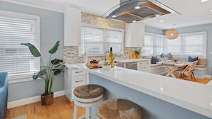 Una cocina moderna con una isla central, armarios blancos y un amplio ventanal con persianas.