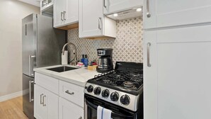A kitchen with white cabinets, a stainless steel refrigerator, a gas stove, and a coffee maker.
