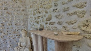 A stone wall with a Buddha statue and a wooden shelf with a cup and a bowl.