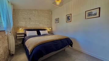 A bedroom with a stone wall, a bed with a headboard, a bedside table with a lamp, and framed pictures on the wall.