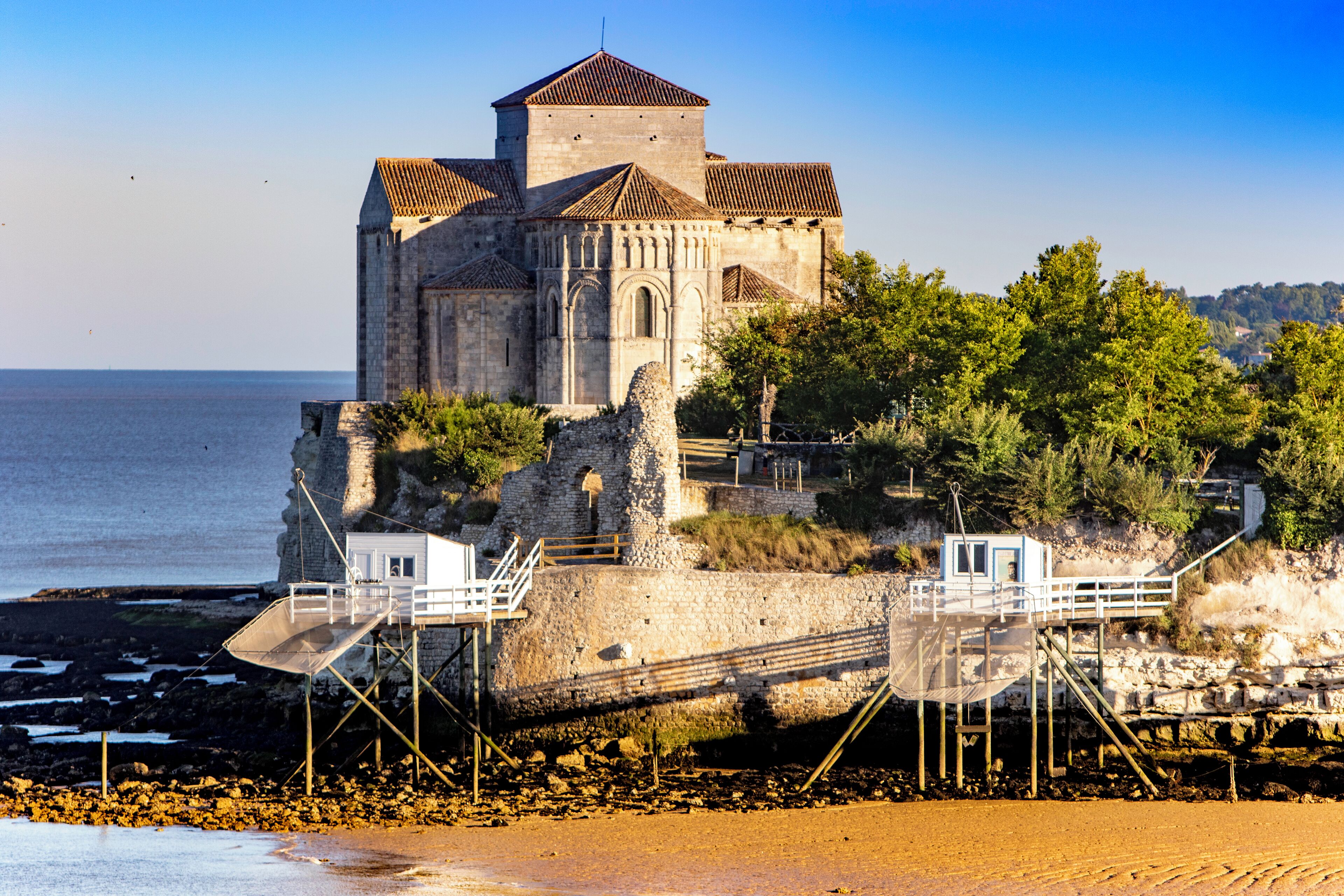 Un edificio de piedra histórico con una torre, ubicado en una costa rocosa con vistas despejadas al mar.