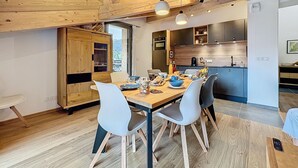 Eine moderne Küche mit Holzbalken, ein Essbereich mit großem Tisch und Stühlen und Blick ins Freie.
