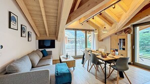 Ein modernes Interieur mit Holzbalkendecke, einer Essecke mit Tisch und Stühlen sowie einem Sofa mit blauem Überwurf.