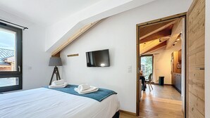 Ein Schlafzimmer mit Bett, einem an der Wand befestigten Fernseher und Blick ins Freie durch ein Fenster.