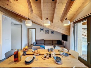 A cozy dining area with a wooden table set for a meal, a sofa in the background, and a TV mounted on the wall. - Les 3 Mousquetons- appartement- 6,8 Pers - Proche (Les Gets)
