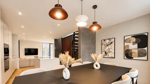 A modern kitchen with a built-in oven, a dining area with a large table and chairs, and a living area with a sofa and a flat-screen TV.