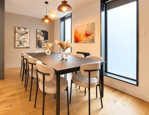 A dining area with a table, chairs, pendant lights, artwork, and a large window. - Luxury Townhouse 4BR I Roof Terrace I Parking (Greater Manchester)