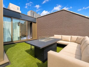 A modern outdoor living space with a glass door leading to a room, a black table, and a beige sofa.