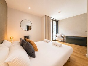 A modern bedroom with a large bed, a round mirror, a fireplace, and a view of the outdoors.