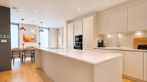 A modern kitchen with a large island, built-in appliances, and a dining area with chairs.