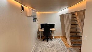 Una oficina en casa con un escritorio, una silla y una computadora, una escalera y una alfombra en el suelo.