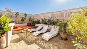 A sunlit outdoor seating area with lounge chairs and a small table, surrounded by potted plants and a lattice fence. - Riad Jarco MARRAKECH, heart medina, Rooftop,  Swimmingpool, Near Jemaa El Fna (Marrakech)