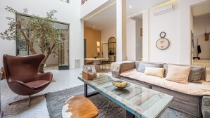 A modern living room with a glass coffee table, leather armchair, and a sofa with cushions. There is a dining area with a table and chairs in the background. - Riad Jarco MARRAKECH, heart medina, Rooftop,  Swimmingpool, Near Jemaa El Fna (Marrakech)