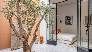 A bedroom with a bed, a glass door, and a tree in a courtyard. - Riad Jarco MARRAKECH, heart medina, Rooftop,  Swimmingpool, Near Jemaa El Fna (Marrakech)