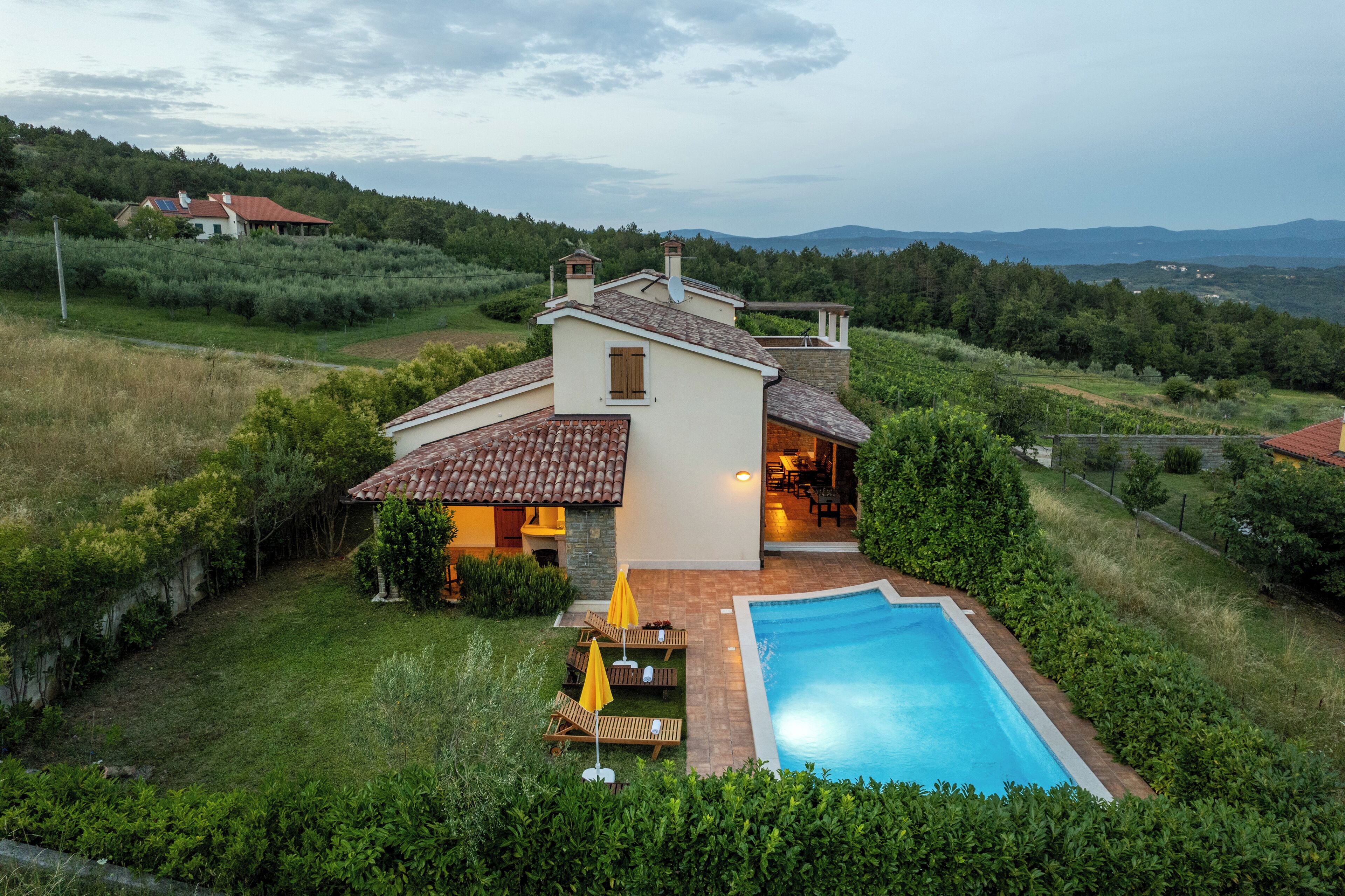 Uma vila com piscina, rodeada por vegetação exuberante e montanhas ao fundo.