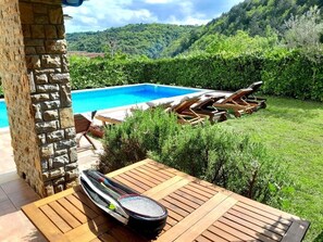 Un área junto a la piscina con un muelle de madera, sillas de descanso y una mesa con una tabla de remo.