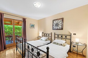 Un dormitorio con dos camas, una ventana con cortinas, una lámpara en el techo e imagen colgada en la pared.