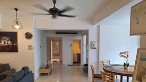 Una sala de estar moderna con un sofá, una mesa de comedor con sillas, un ventilador de techo y una cocina al fondo.