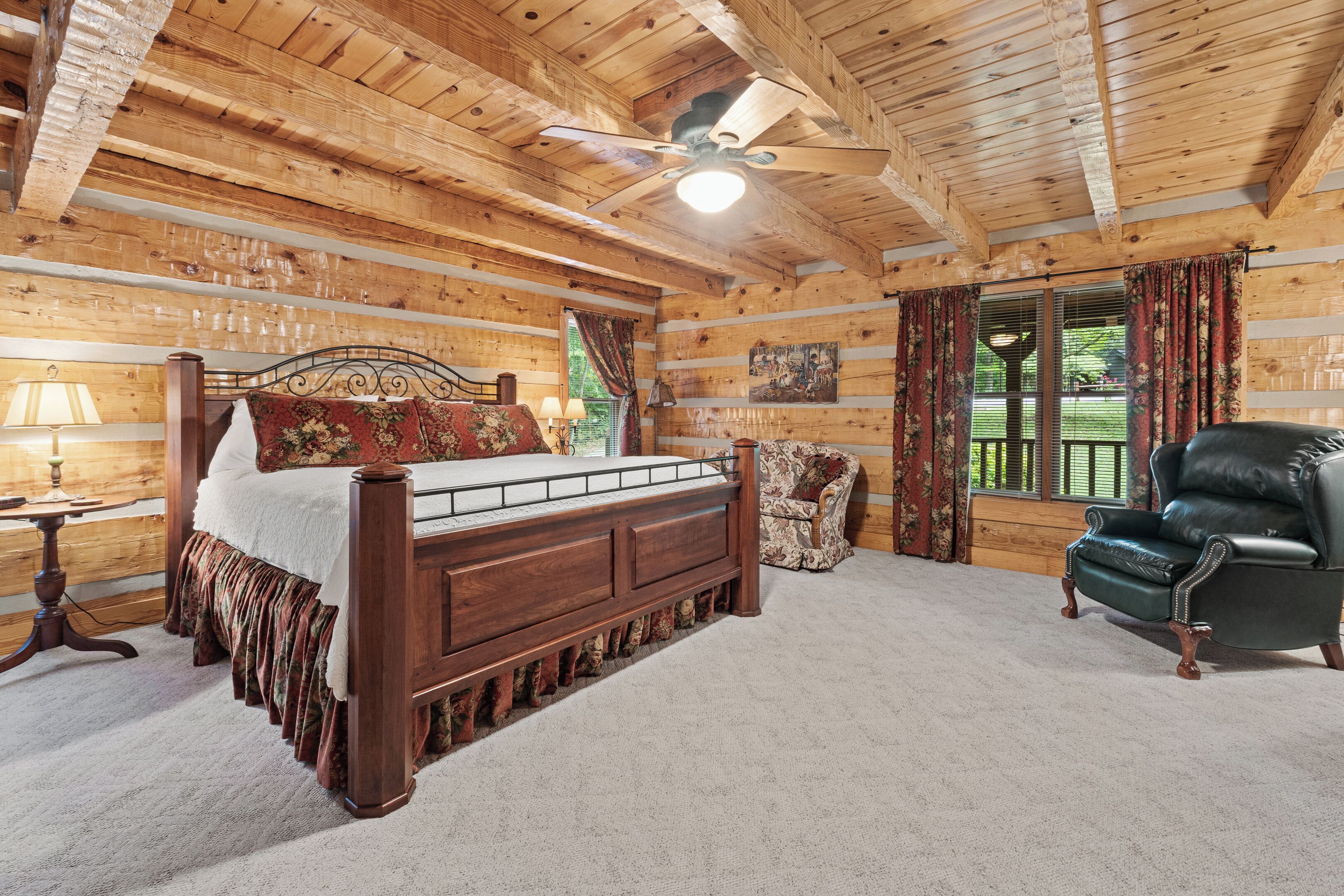 A log cabin bedroom with a wooden bed, a leather armchair, and a ceiling fan.