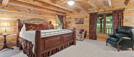 A log cabin bedroom with a wooden bed, a leather armchair, and a ceiling fan.