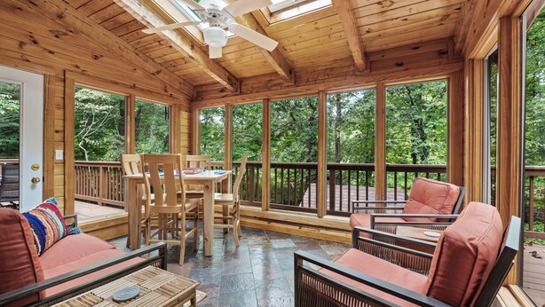 Eine Holzterrasse mit Tisch und Stühlen, großen Fenstern und einem Deckenventilator.
