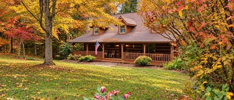 A log cabin with a porch, surrounded by autumn foliage.