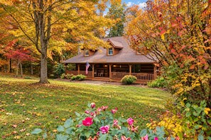 A log cabin with a porch, surrounded by autumn foliage.