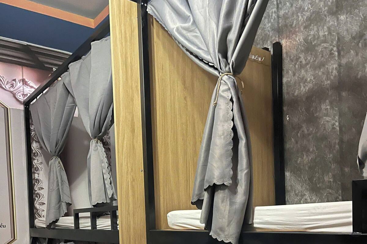 Ein Stockbett mit grauen Vorhängen, die an den Ecken gebunden sind, ein hölzernes Kopfteil und ein kleiner Tisch mit weißem Tuch.