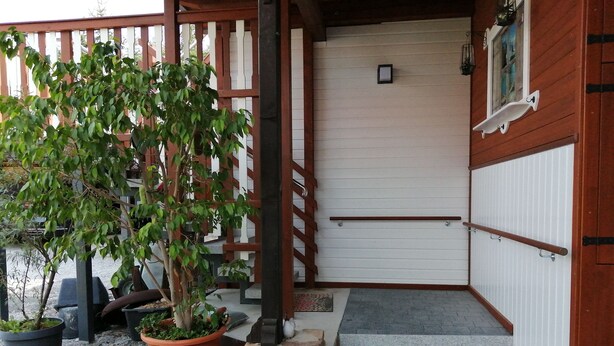 A wooden gate leading to a building with a white exterior and a stone wall. There is a potted plant on the ground. - Ferienwohnung "alte Ziegelei 2" Benzingerode ist ein Ortsteil von Wernigerode (Wernigerode)