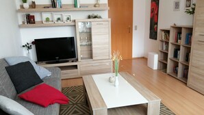 A modern living room with a grey sofa, a flat-screen TV, wooden shelves, a coffee table, and a bookshelf. - Ferienwohnung "alte Ziegelei 2" Benzingerode ist ein Ortsteil von Wernigerode (Wernigerode)