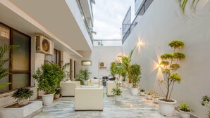 A spacious indoor courtyard with potted plants, seating areas, and a high ceiling. - Hotel Ashiyana Elite (Gurugram)