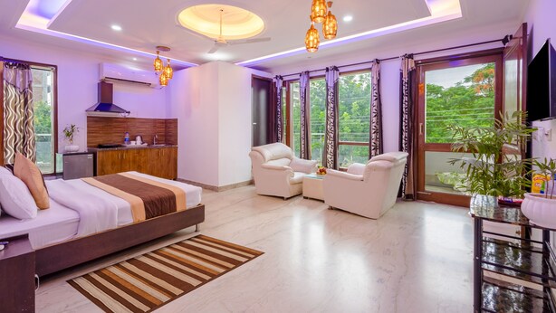 A modern bedroom with a bed, seating area, and a view of greenery. - Hotel Ashiyana Elite (Gurugram)