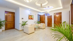 A modern hotel lobby with a marble floor, white sofas, a glass coffee table, and wooden doors numbered 105 and 102. - Hotel Ashiyana Elite (Gurugram)
