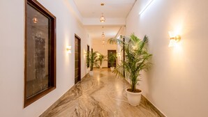 A hallway with marble flooring, potted plants, and wall-mounted lighting fixtures. - Hotel Ashiyana Elite (Gurugram)