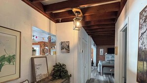 A hallway with wooden beams, a wooden bench, framed artwork, and a hanging light fixture. - Lakefront Bliss | Kayaks • Paddleboards • Fire Pit • Snowbird Specials (Melrose)