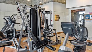Een sportschool met diverse fitnessapparaten, een bord aan de muur en een deur met een waarschuwingsbord.