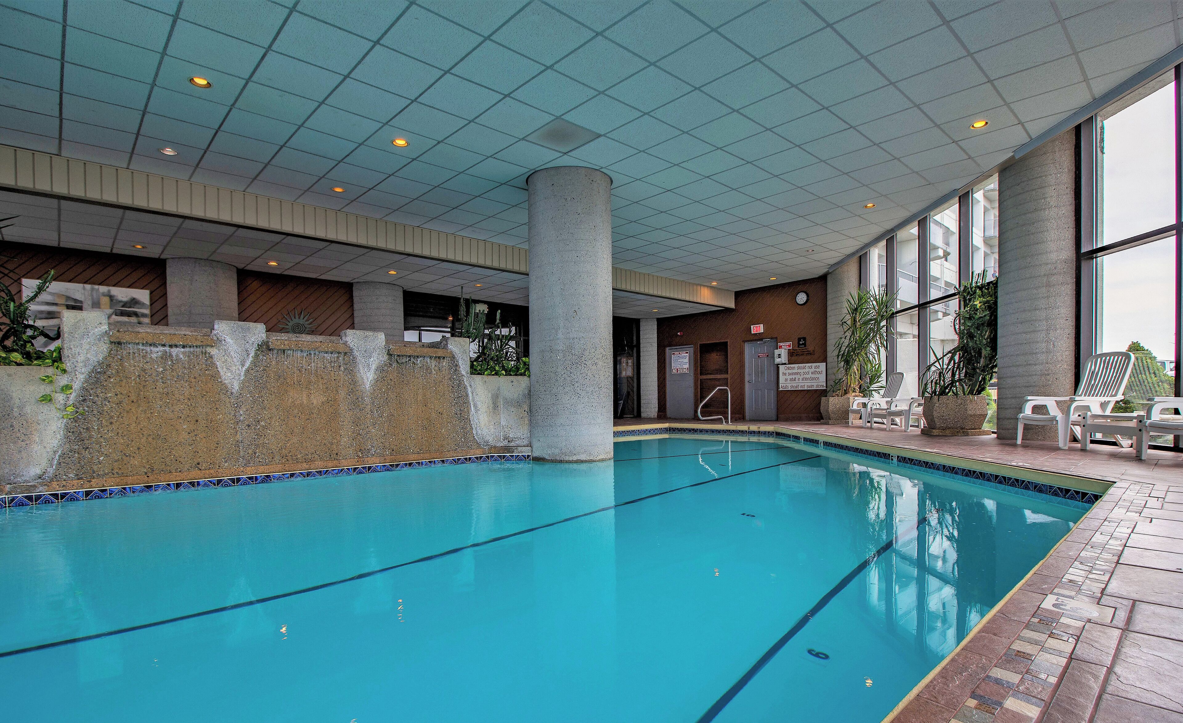 An indoor swimming pool with clear water, a tiled floor, and a few lounge chairs.
