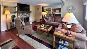 Ein Wohnzimmer mit Kamin, Fernseher und einer Küche im Hintergrund.