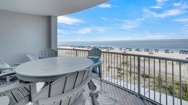 Un balcon avec une table et des chaises, donnant sur une plage parsemée de parasols et de chaises longues.