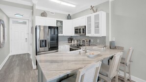 Une cuisine moderne avec des meubles blancs, des appareils en acier inoxydable et un plan de travail en marbre.