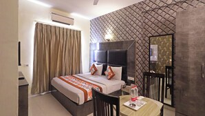 A hotel room with a bed, a desk, a chair, a table, a ceiling fan, and a wall-mounted TV. - Hotel Smart Lax (New Delhi)