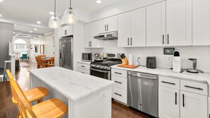 A modern kitchen with white cabinets, stainless steel appliances, and a marble island with bar stools.